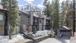 Un edificio residencial de varios pisos con vistas a la montaña, una pequeña construcción tipo cabaña y una escalera que lleva a los pisos superiores.
