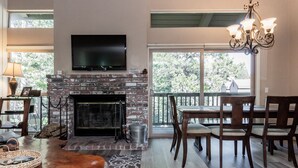 Una sala de estar con chimenea, un televisor montado encima y un comedor con sillas de madera y una mesa.