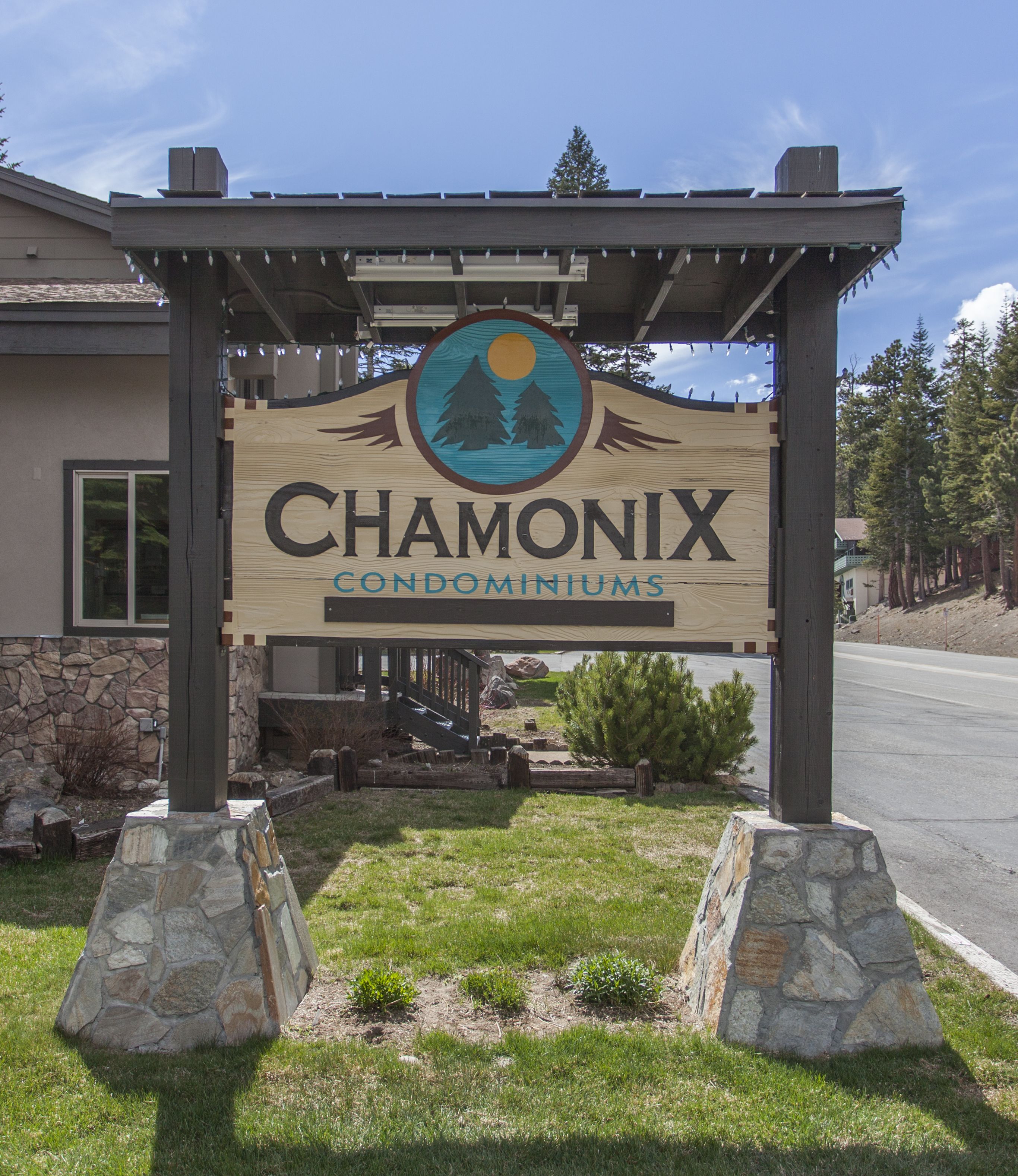 Une enseigne en bois indiquant « Chamonix Condominiums », avec un logo représentant une montagne et un arbre.
