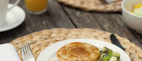 A breakfast setting with pancakes, kiwi, and orange juice on a wooden table.