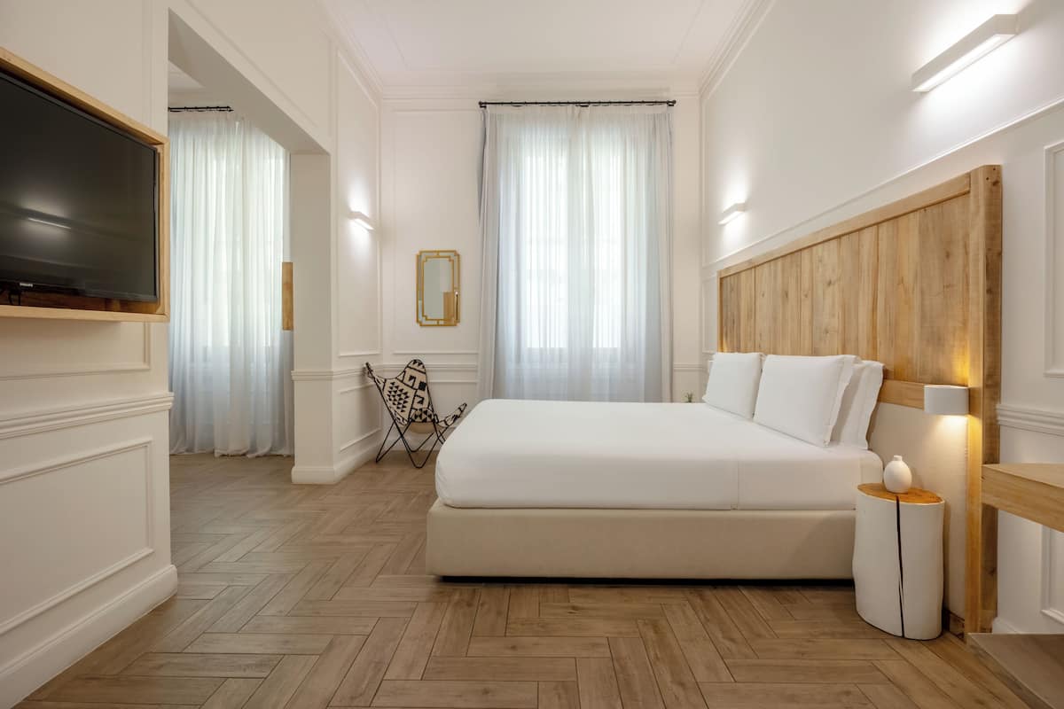 A bedroom with a large bed, a TV mounted on the wall, a wooden headboard, and a small side table.