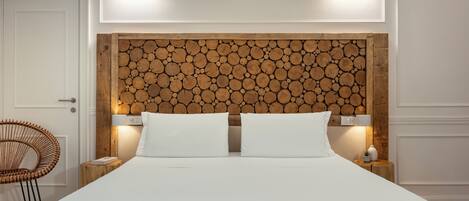 Una cama bien hecha con sábanas blancas, cabecera de madera con diseño de troncos, lámparas de noche y una silla de mimbre.