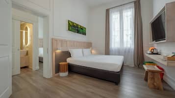 Una habitación de hotel con cama, televisión, un cuadro, ventana con cortinas y suelo de madera.