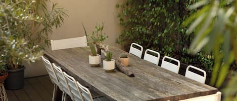 A wooden table with six white chairs, surrounded by potted plants and a wall of greenery.