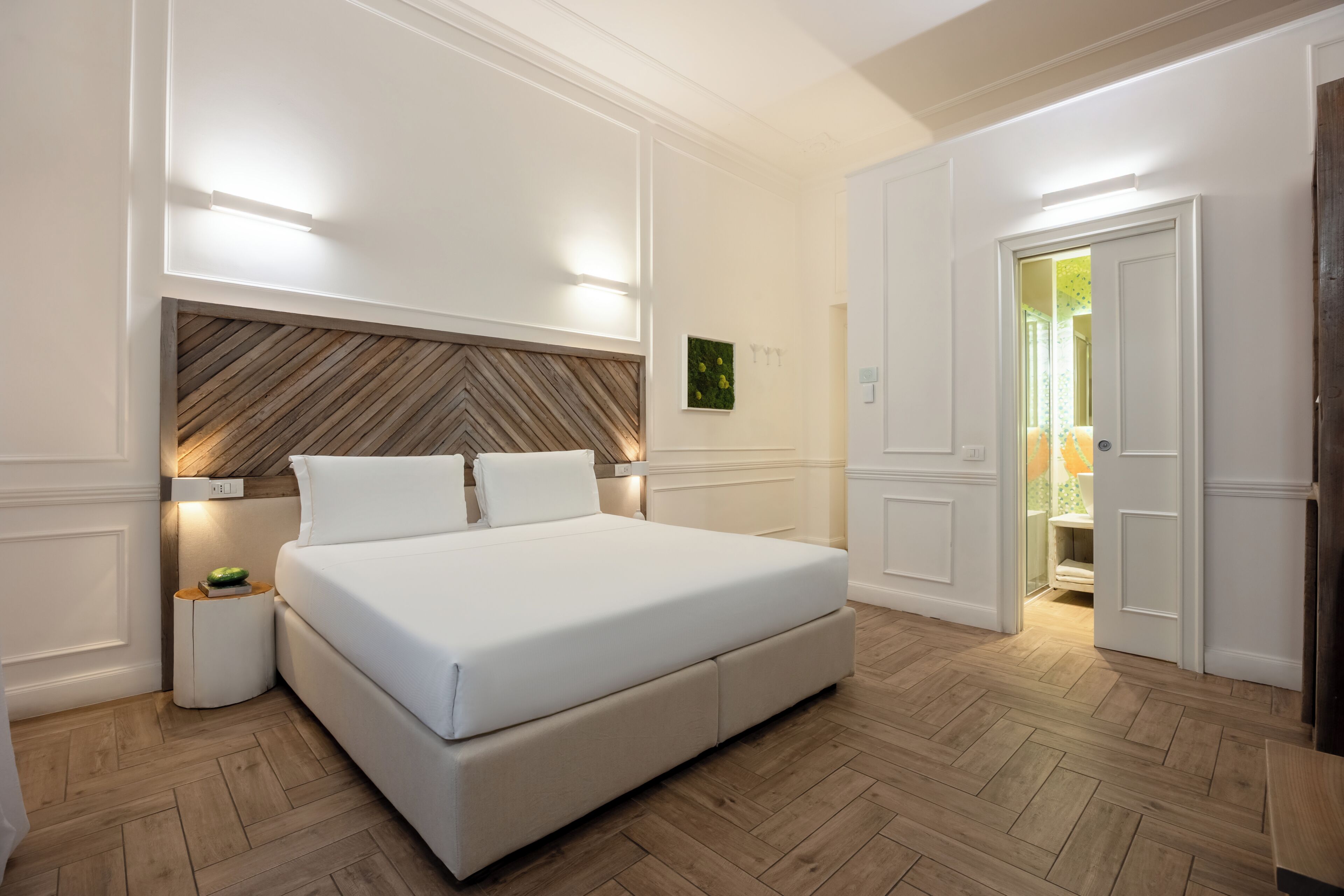 Ein Schlafzimmer mit einem großen Bett, einem Holzkopfende, Nachttischlampen und einem Parkettboden mit Fischgrätmuster.