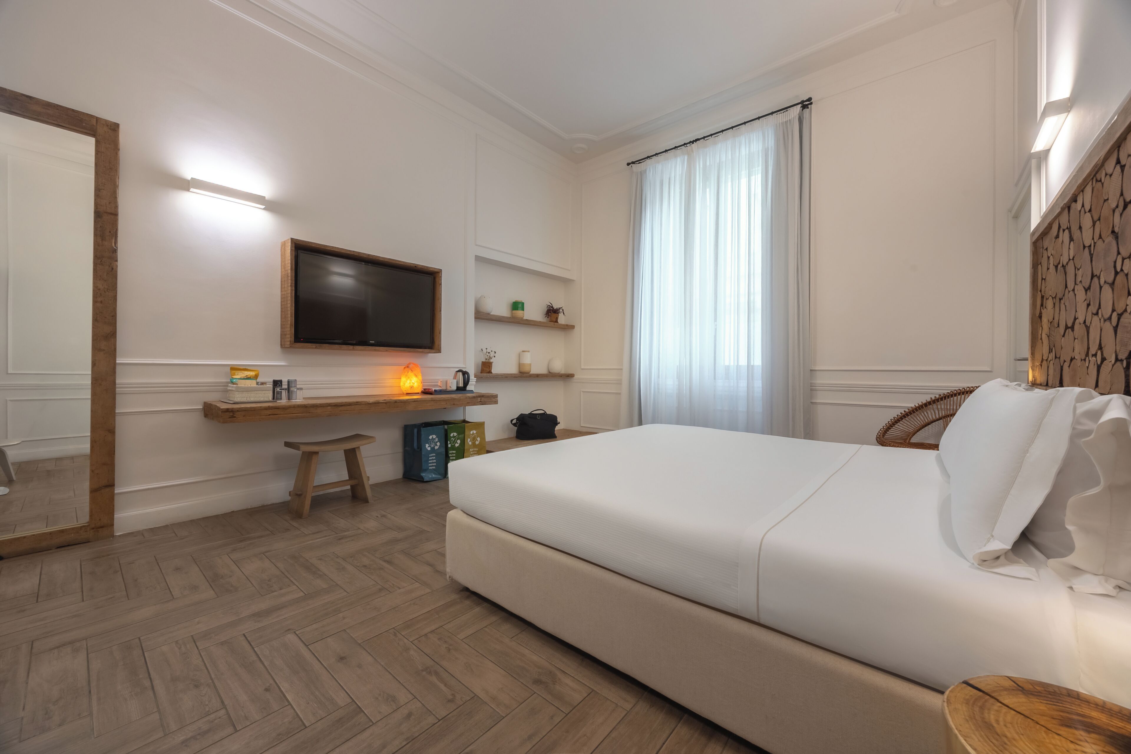 Una habitación de hotel moderna con cama, escritorio, televisión y un amplio ventanal con cortinas.