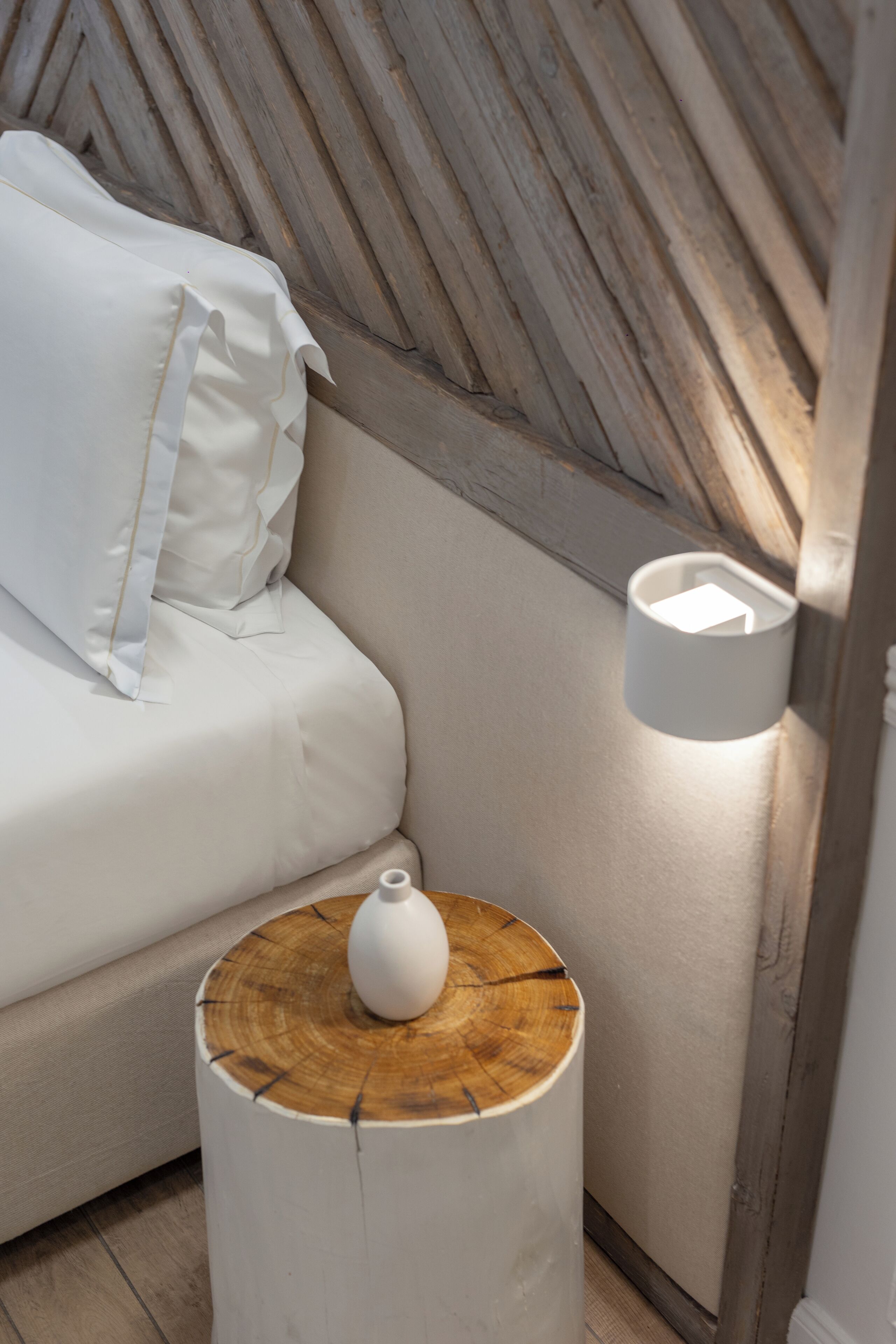 Un lit avec un oreiller blanc et une table de chevet sur laquelle se trouve un vase.