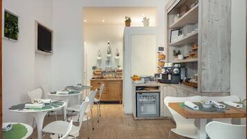 Une cuisine moderne avec des meubles blancs, un réfrigérateur et un coin repas comprenant des chaises et des tables blanches.