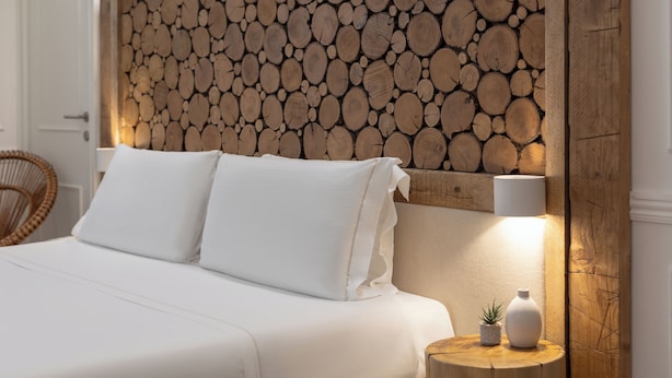 A bed with white bedding, a wooden headboard with logs, a bedside table with a lamp, and a small plant. - Eco Urban B&B (Florence)