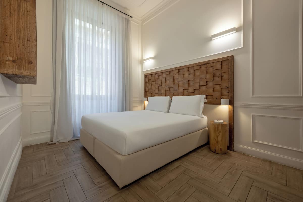 A bedroom with a wooden headboard, a bed, a bedside table, and a window with curtains.