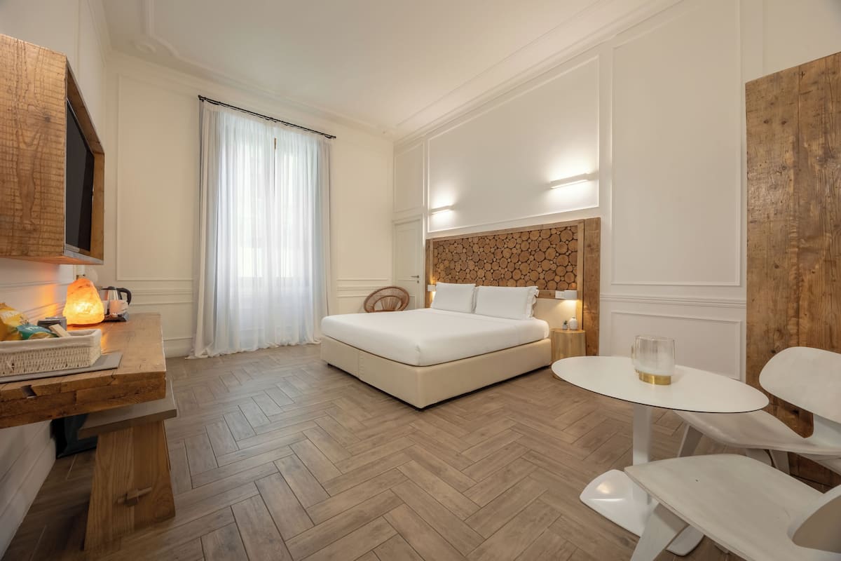 A hotel room with a bed, a desk with a lamp, a chair, and a small table.