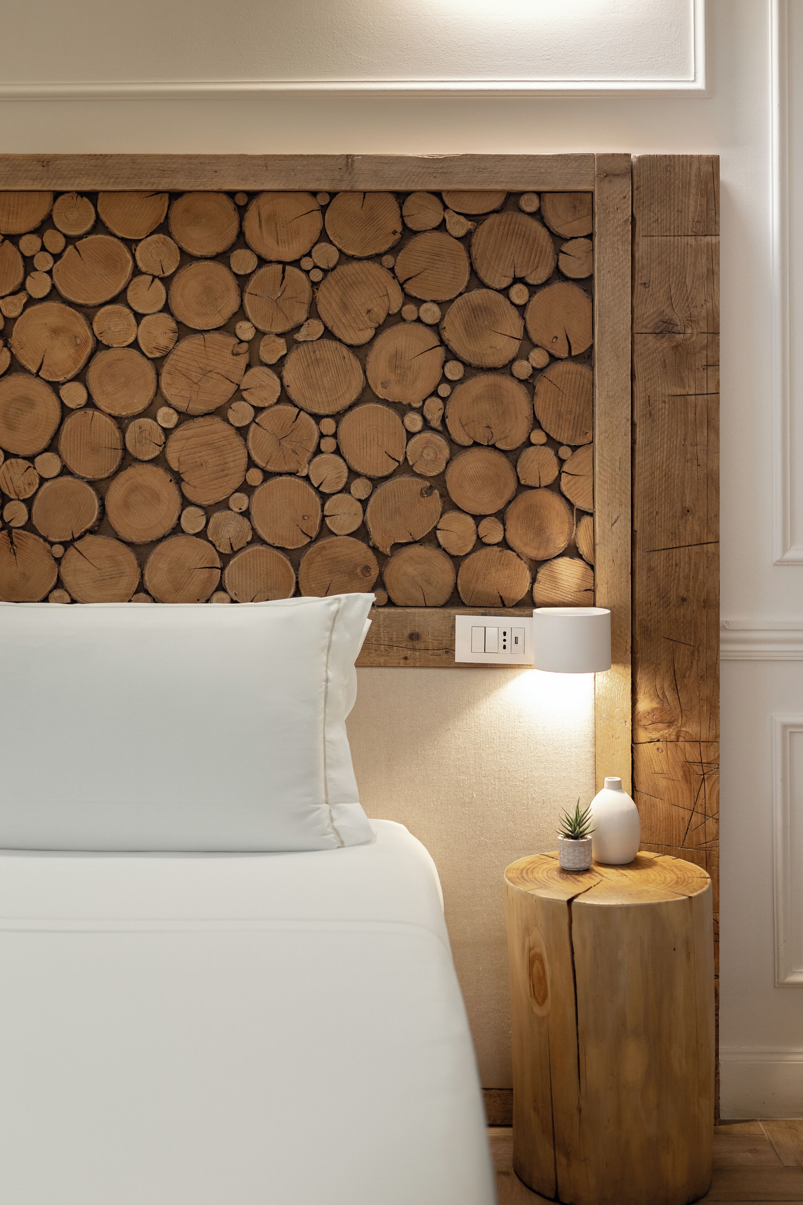 Un dormitorio con pared de troncos de madera, una lámpara de noche, una planta pequeña y un enchufe.