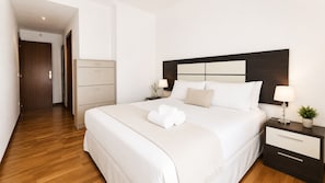 Habitación de hotel con una cama grande, una mesita de noche con lámpara, una planta pequeña y suelo de madera.