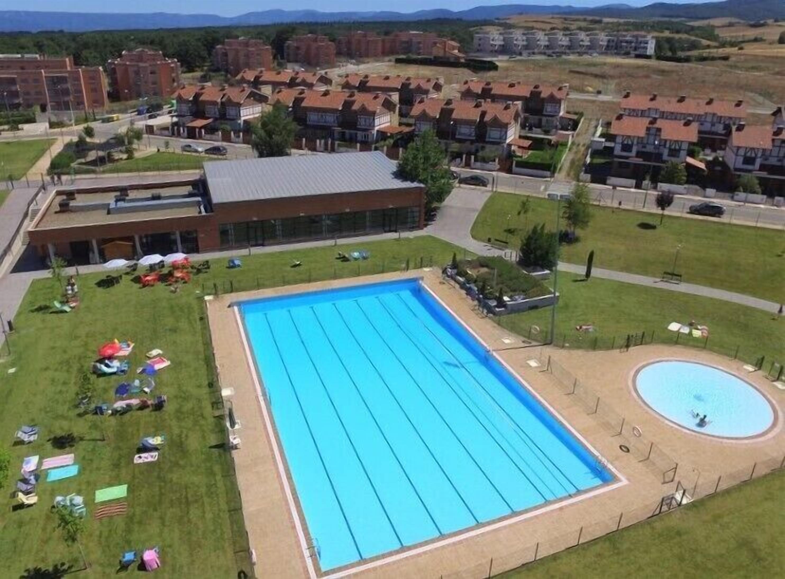 A large rectangular swimming pool with a smaller circular pool, surrounded by a grassy area with umbrellas and lounge chairs.