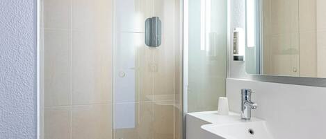 Un baño moderno con cabina de ducha de vidrio, un lavamanos blanco y un espejo grande.