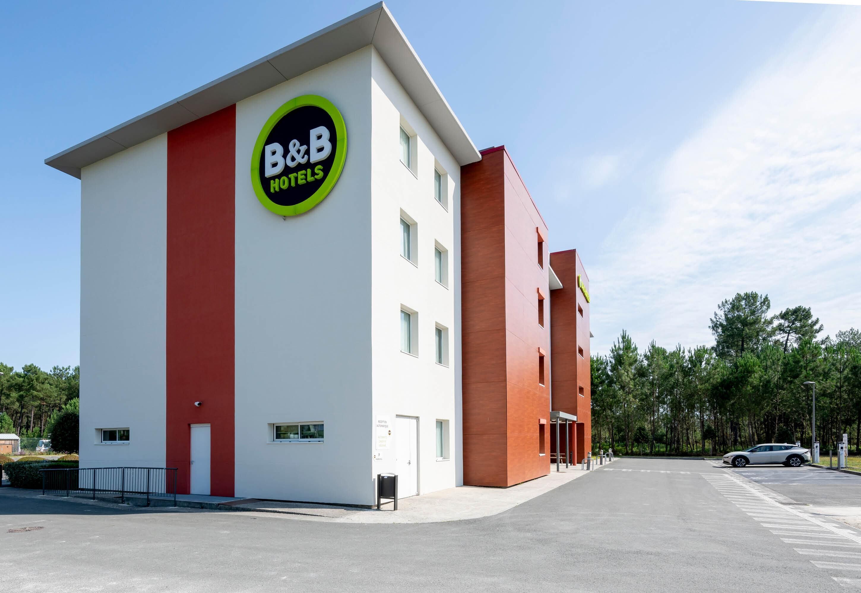 A B&B hotel with a prominent sign, a parking lot, and a clear sky.
