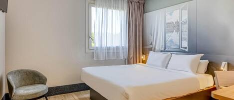 Una habitación de hotel con una cama, una silla, un escritorio y un ventanal con cortinas.