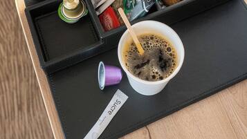 Een koffieapparaat met een dienblad met een kop koffie, een blikje frisdrank, een pak koekjes, een waterfles en een koffiemok.