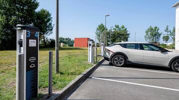 Un espace de stationnement équipé de bornes de recharge pour véhicules électriques, une voiture et un bâtiment en arrière-plan.