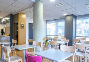 Un comedor moderno con varias mesas y sillas, un pilar grande y vistas de la ciudad a través de amplias ventanas.