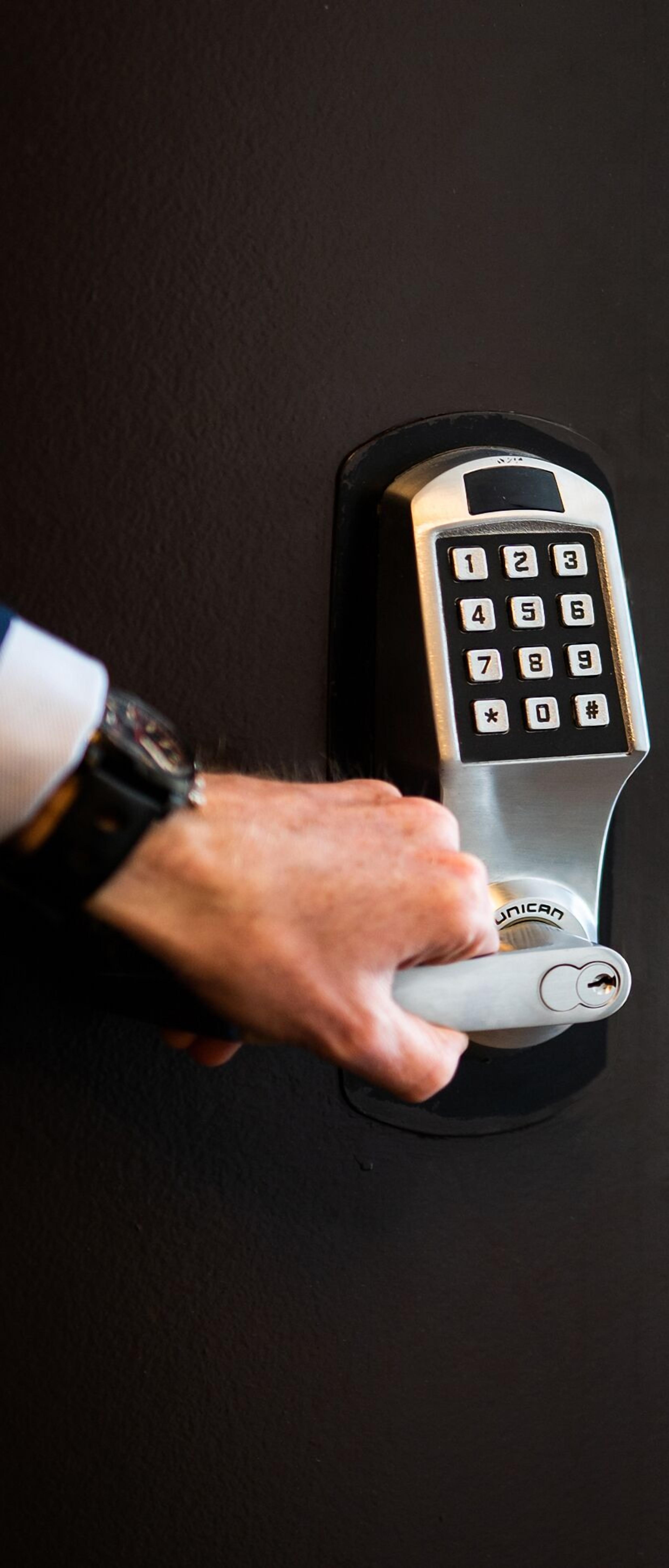 A hand pressing a key on a wall-mounted telephone.