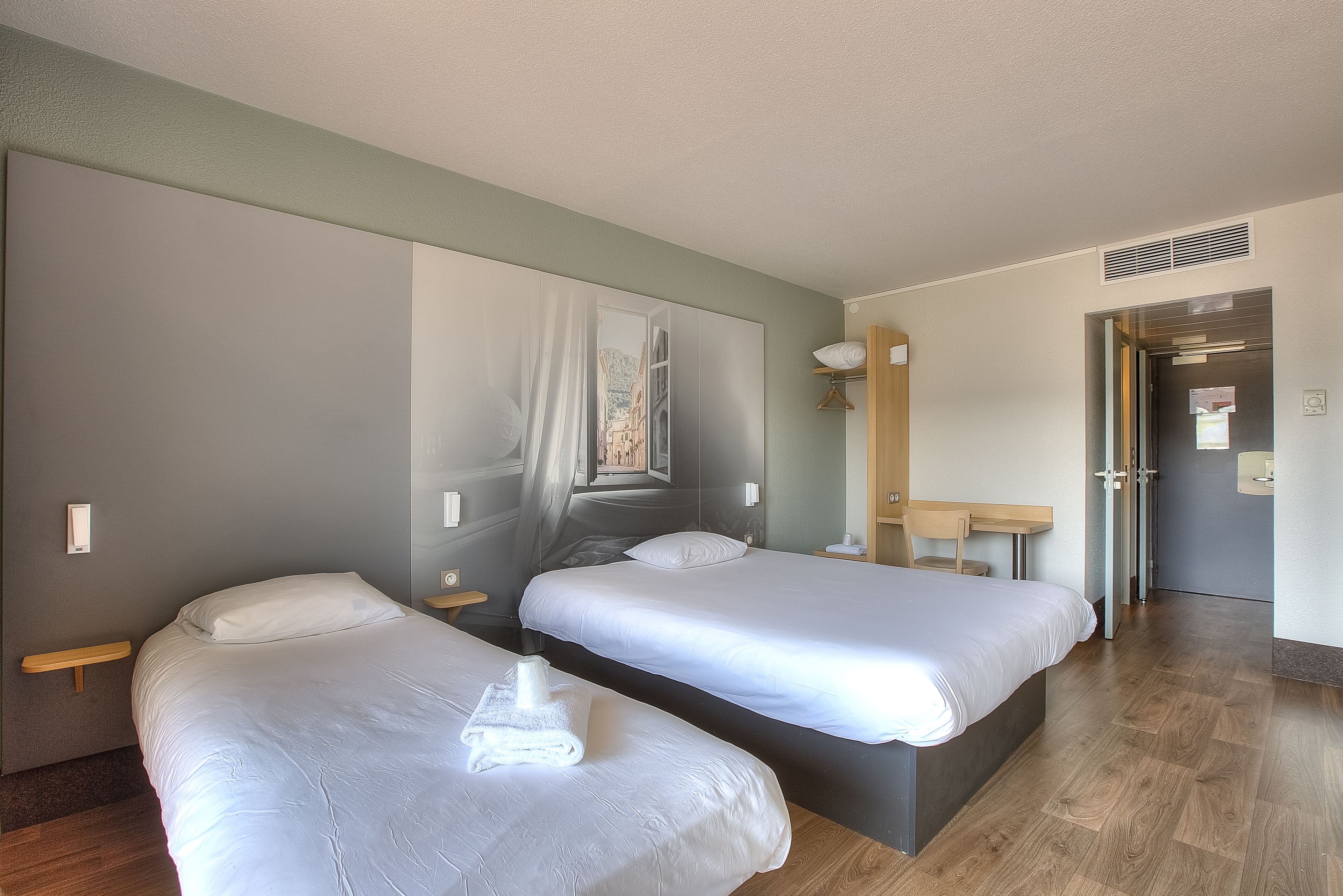 A hotel room with two beds, a large wall mural, a wooden floor, and a small desk with a chair.