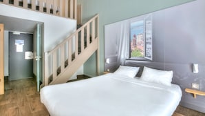 Ein Hotelzimmer mit einem großen Bett, einem Fenster mit Blick auf die Stadt, einer Treppe und einer Tür.
