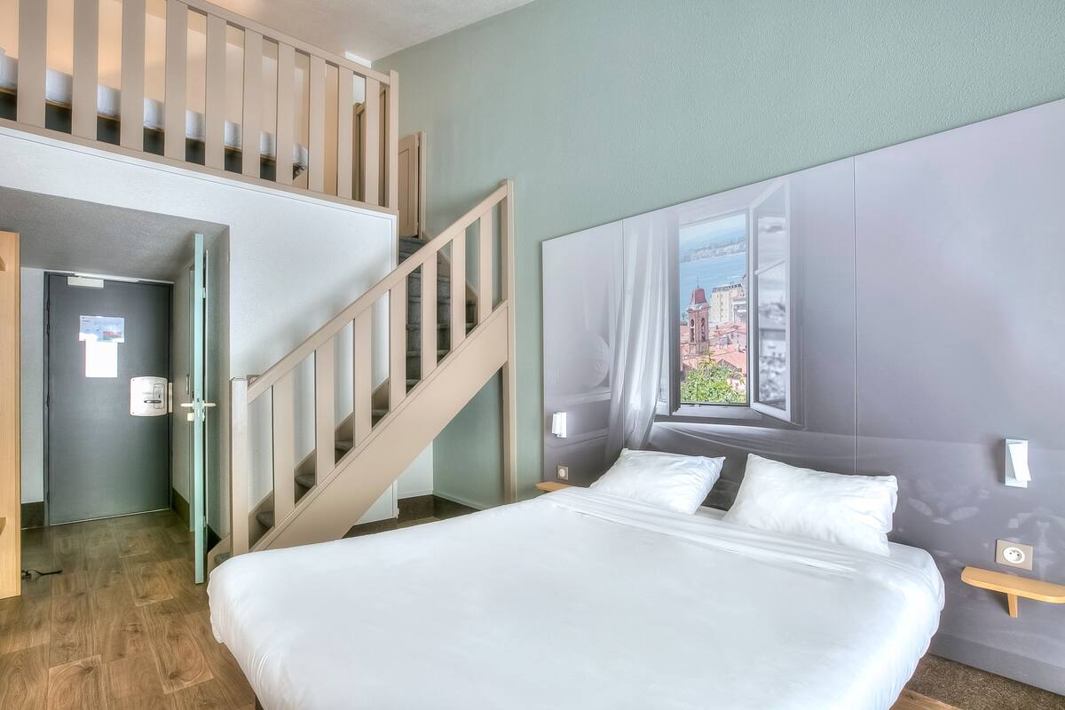 Habitación de hotel con una cama grande, una ventana con vistas a la ciudad, una escalera y una puerta.