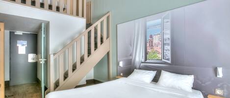 A hotel room with a large bed, a window with a city view, a staircase, and a door.