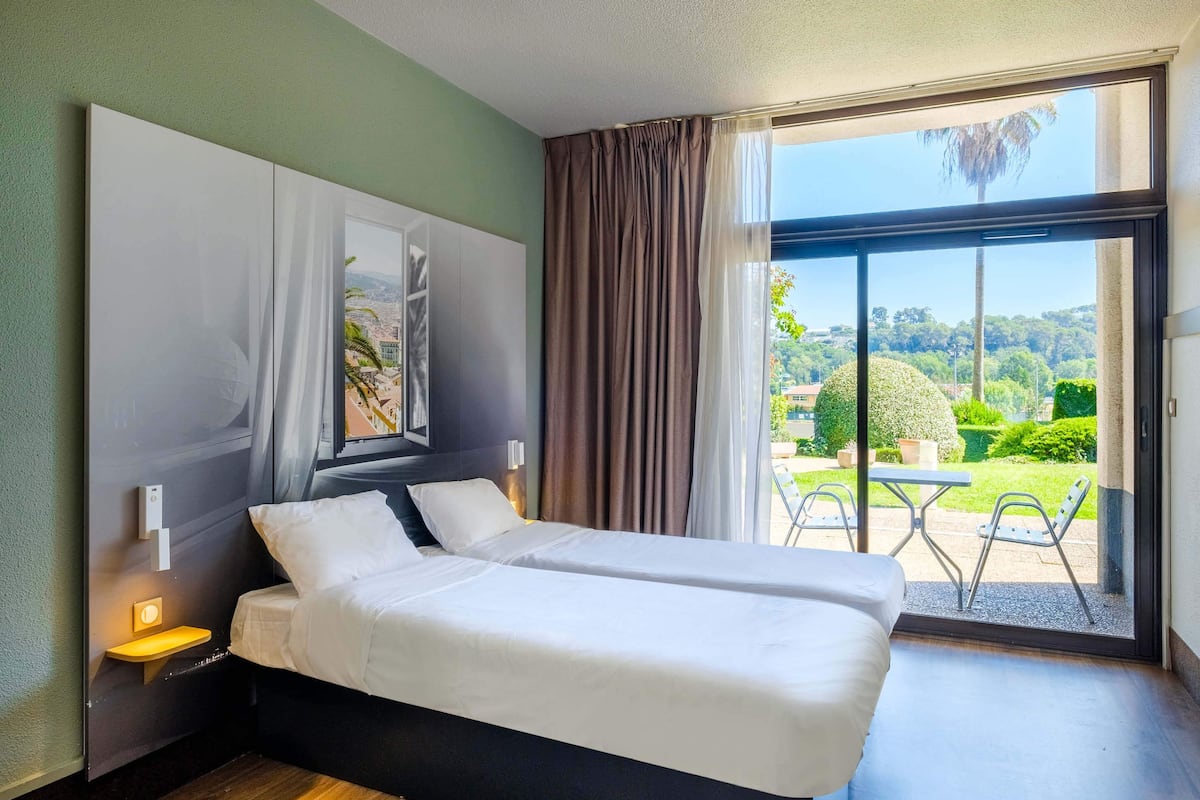 Habitación de hotel con cama, mesita de noche, ventana con cortinas y vista al exterior.