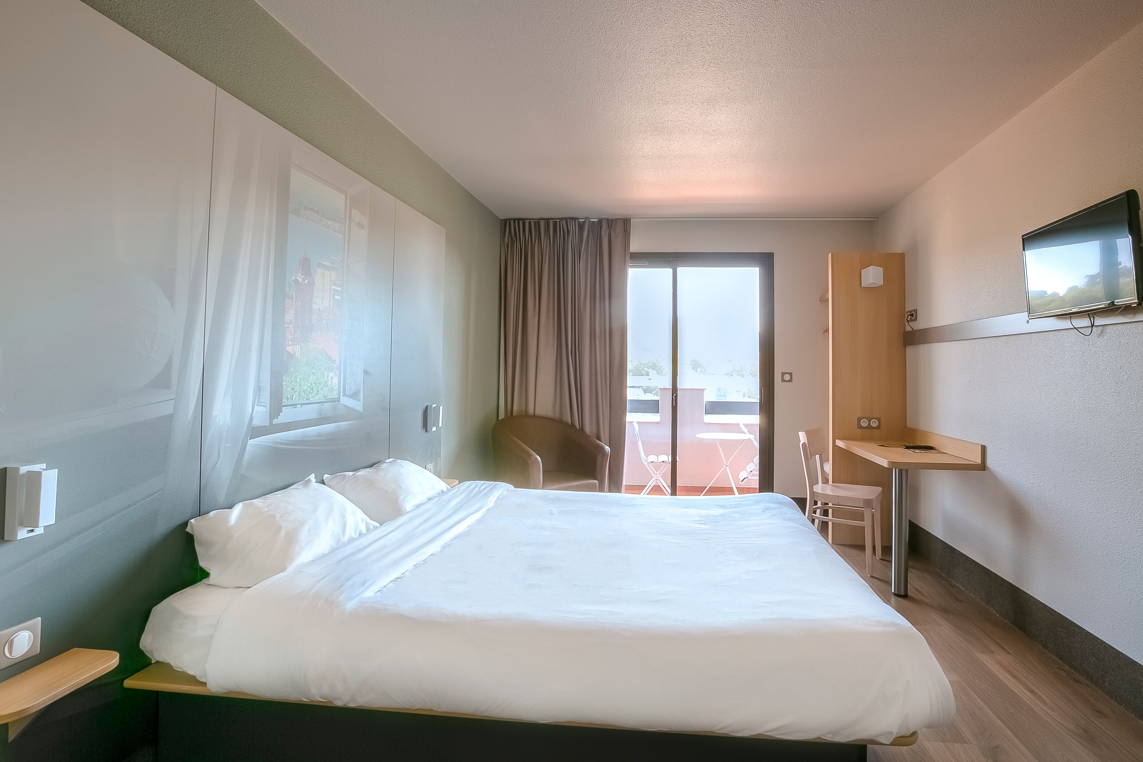 Une chambre d’hôtel avec un lit, un bureau, une chaise et un téléviseur fixé au mur.