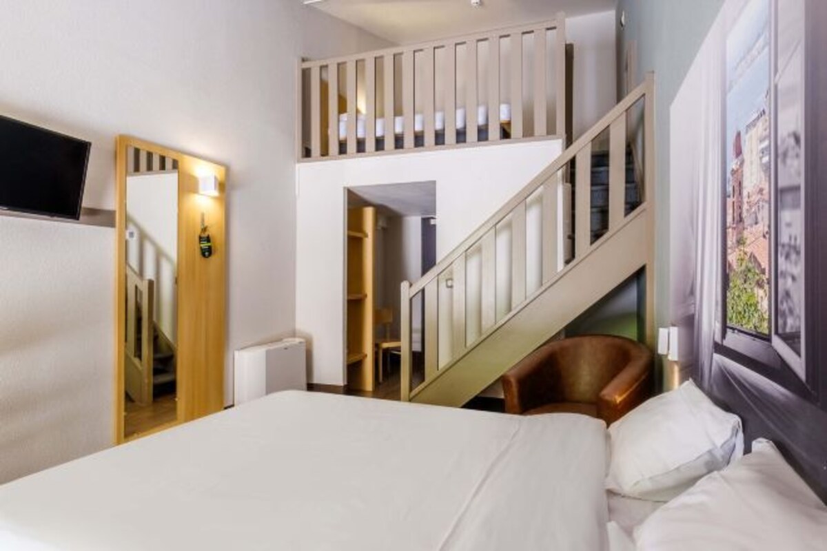Un dormitorio con una cama, una silla, una escalera y un televisor montado en la pared.