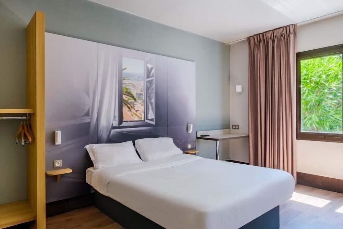 Habitación de hotel moderna con cama, escritorio y vistas a zonas verdes por la ventana.