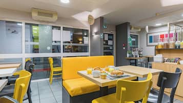 Een restaurant met gele zitbanken en tafels, een ontbijtbuffet en uitzicht op de straat.