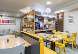 A modern café with yellow and white seating, a coffee machine, and a menu board. - B&B Hotel Tours Sud Joué-lès-tours (Joue-les-Tours)