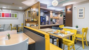 A modern café with yellow and white seating, a coffee machine, and a menu board. - B&B Hotel Tours Sud Joué-lès-tours (Joue-les-Tours)