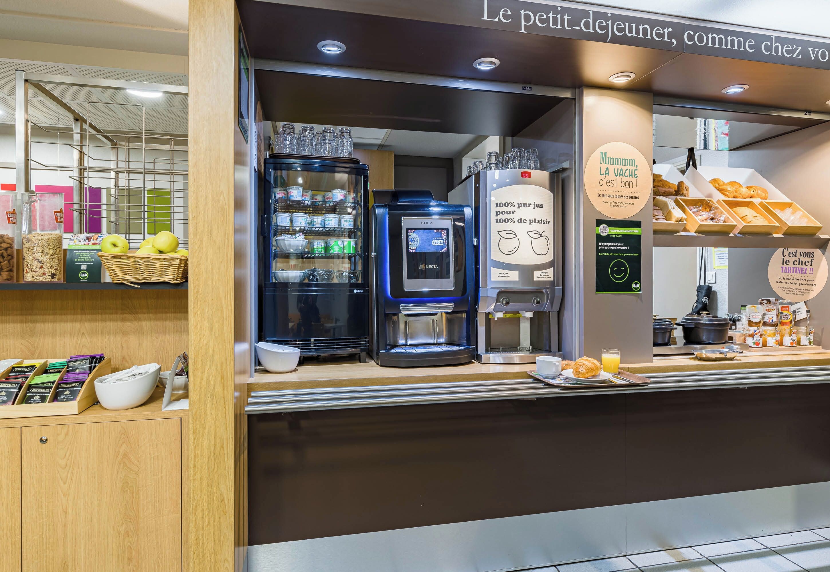 A breakfast counter with coffee machines, a refrigerator, and a display of pastries.
