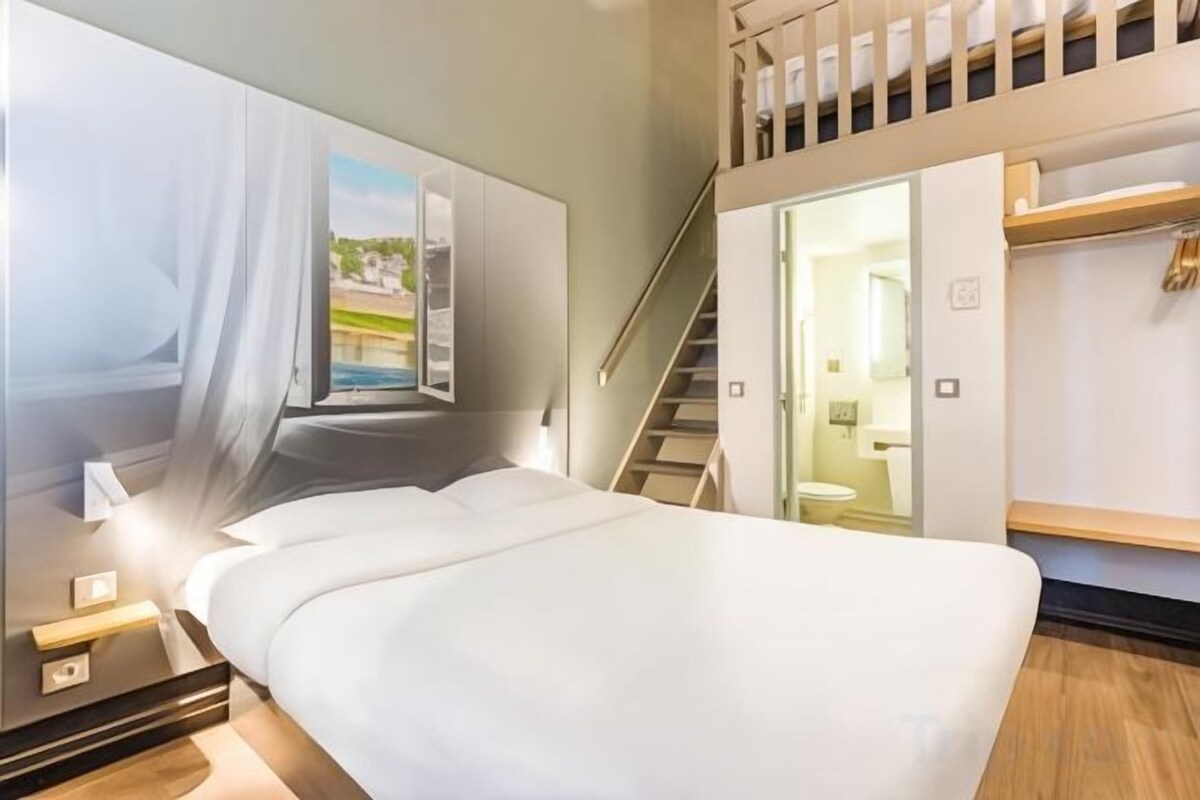 A modern hotel room with a large bed, a view of a balcony, and a staircase leading to an upper level.