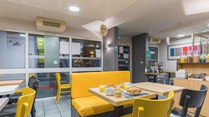 A restaurant with yellow chairs and tables, a counter with food items, and a menu display. - B&B Hotel Tours Sud Joué-lès-tours (Joue-les-Tours)