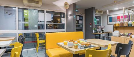 A restaurant with yellow chairs and tables, a counter with food items, and a menu display.