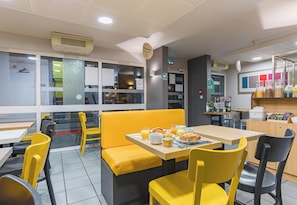 A restaurant with yellow chairs and tables, a counter with food items, and a menu display. - B&B Hotel Tours Sud Joué-lès-tours (Joue-les-Tours)