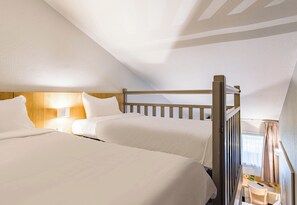 Ein Hotelzimmer mit zwei Betten, Holz-Kopfteilen, einem kleinen Tisch und einem Fenster mit Vorhängen.