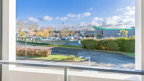 A parking lot with cars, a building with a green roof, and a clear blue sky. - B&B Hotel Tours Sud Joué-lès-tours (Joue-les-Tours)