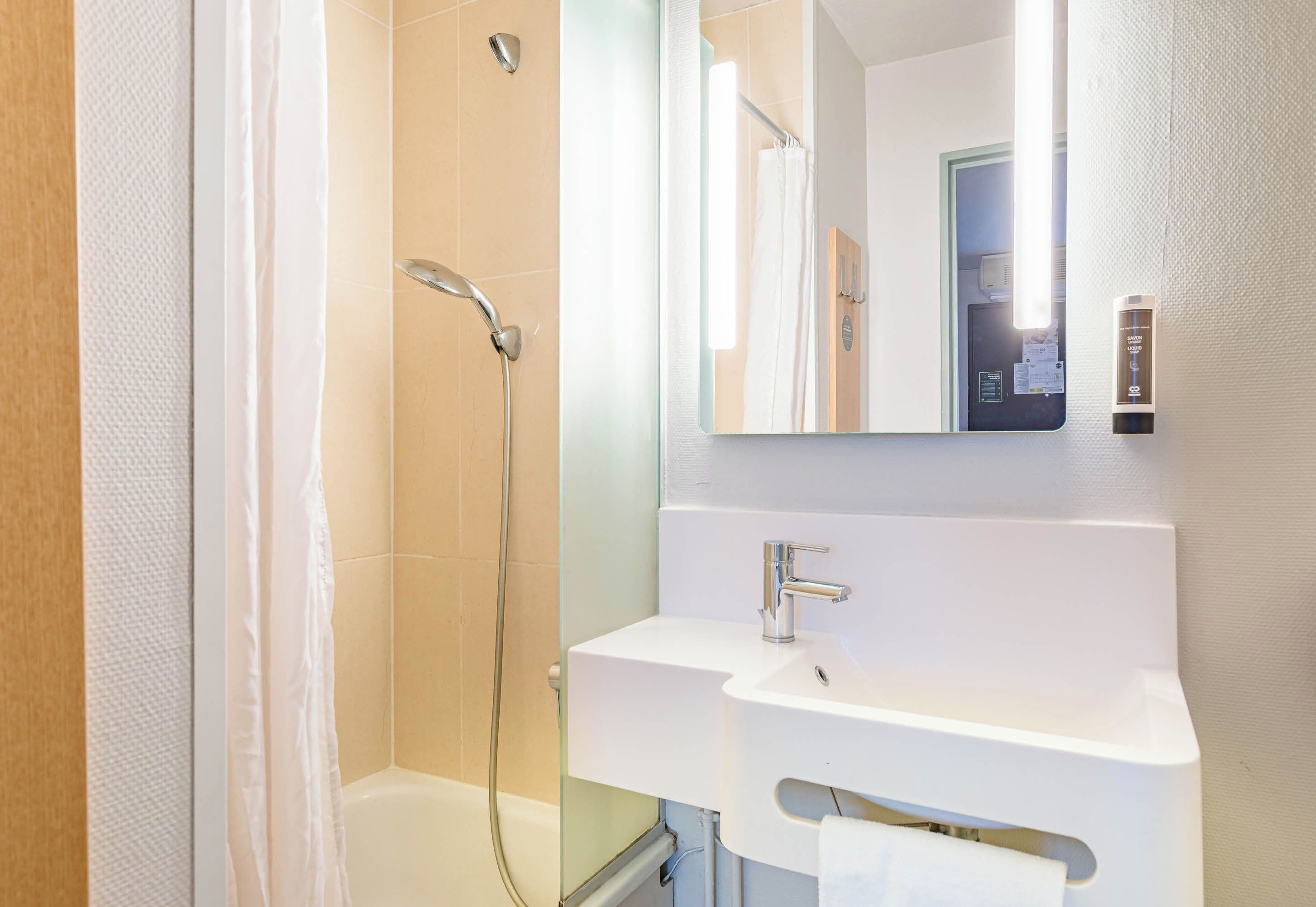 Un baño moderno con ducha de vidrio, un lavamanos blanco y un espejo encima.