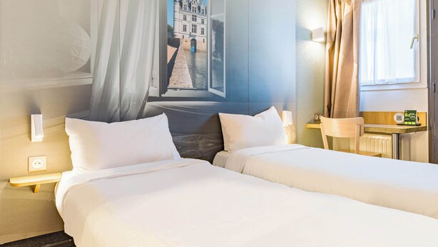 A hotel room with two beds, a large window with curtains, a wall-mounted clock, and a small table with a lamp. - B&B Hotel Tours Sud Joué-lès-tours (Joue-les-Tours)