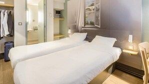 A hotel room with two beds, a wardrobe, a mirror, a window with a view, and a bedside table with a lamp. - B&B Hotel Tours Nord 1 Val De Loire (Tours)