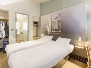 A hotel room with two beds, a wardrobe, a mirror, a window with a view, and a bedside table with a lamp. - B&B Hotel Tours Nord 1 Val De Loire (Tours)