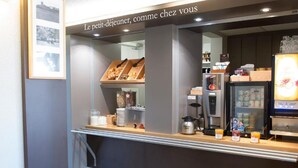 A breakfast counter with croissants, juice, and coffee, and a sign above reading 'Le petit-déjeuner, comme chez vous'. - B&B Hotel Tours Nord 1 Val De Loire (Tours)