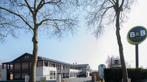 A B&B hotel with a two-story building, a covered parking area, and a sign indicating the hotel's name. - B&B Hotel Tours Nord 1 Val De Loire (Tours)