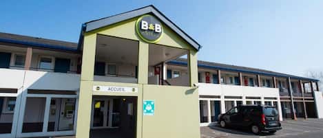 A B&B with a sign for the ACCUEIL, a parking lot, and a building in the background.